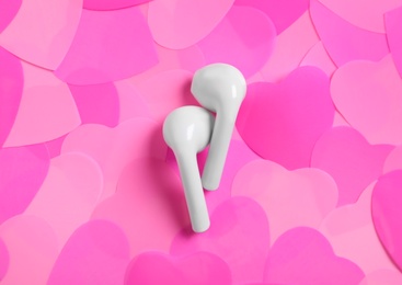 Photo of Modern earphones on pile of pink hearts, flat lay. Listening love music songs
