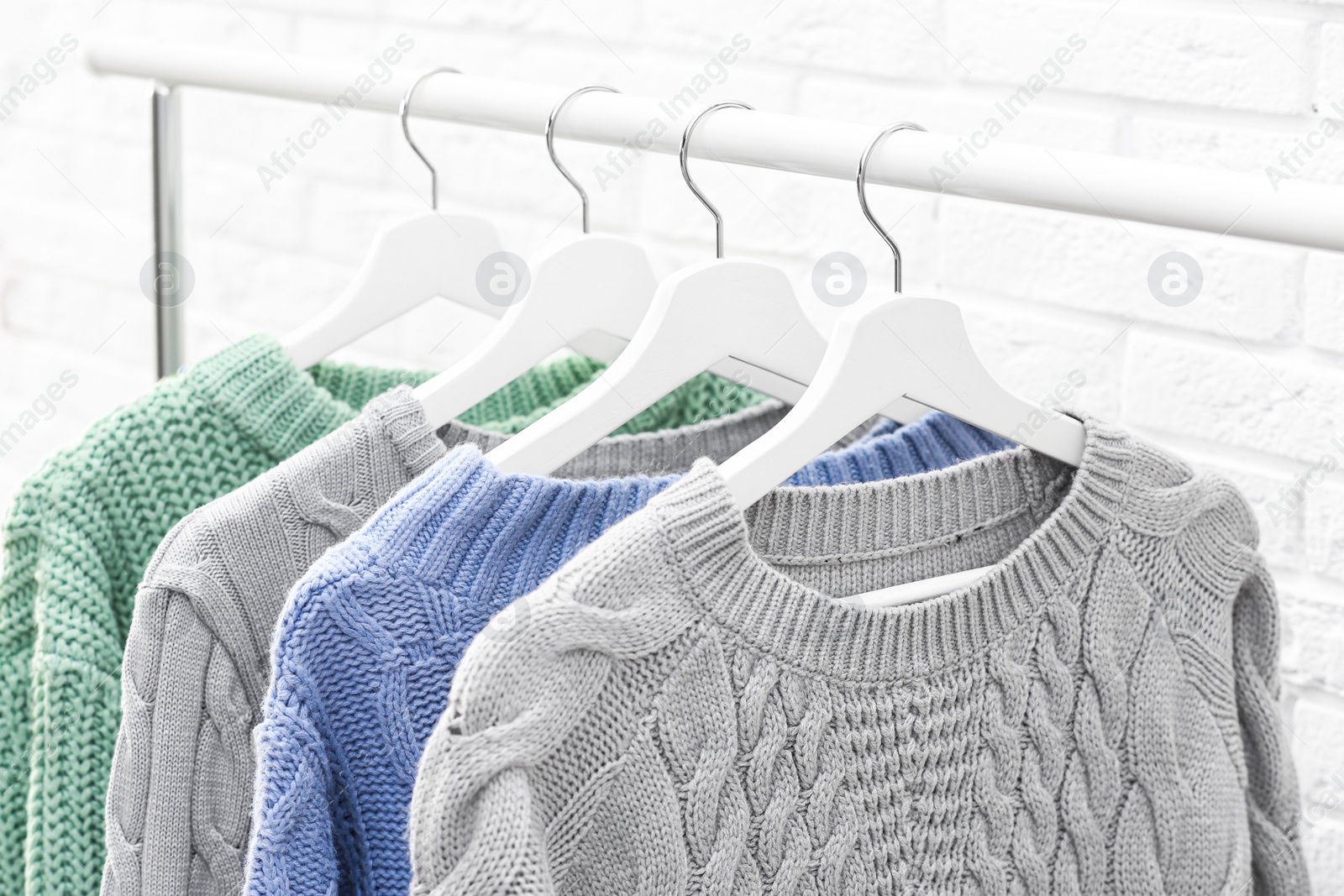 Photo of Collection of warm sweaters hanging on rack near brick wall, closeup