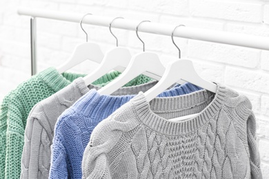 Collection of warm sweaters hanging on rack near brick wall, closeup