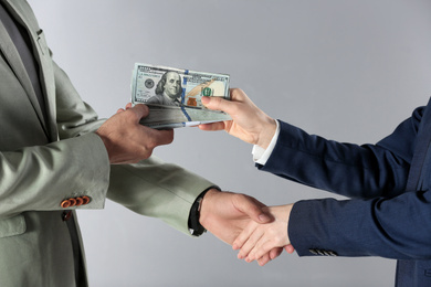 Photo of Woman shaking hands with man and offering bribe on grey background, closeup