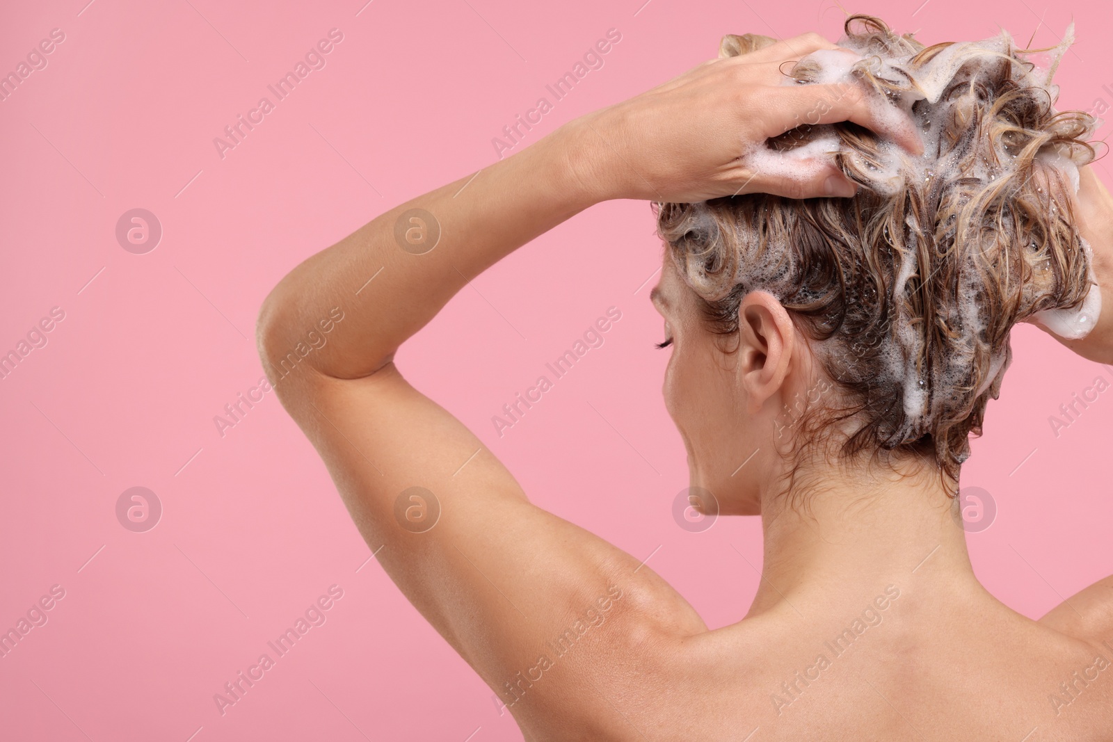 Photo of Woman washing hair on pink background, back view. Space for text