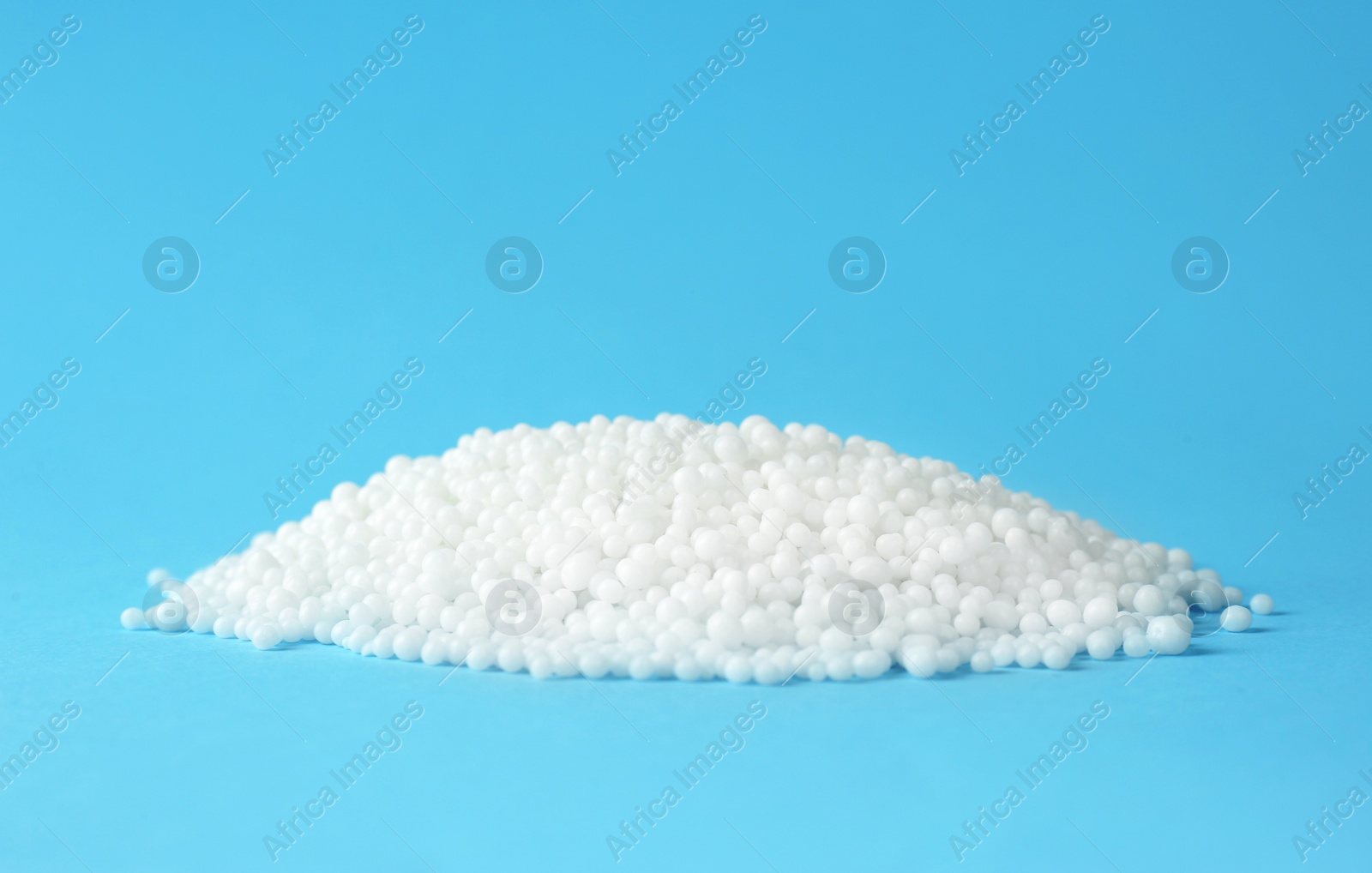 Photo of Pellets of ammonium nitrate on light blue background, space for text. Mineral fertilizer