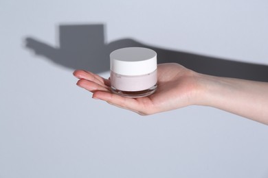 Woman holding jar of cream on grey background, closeup