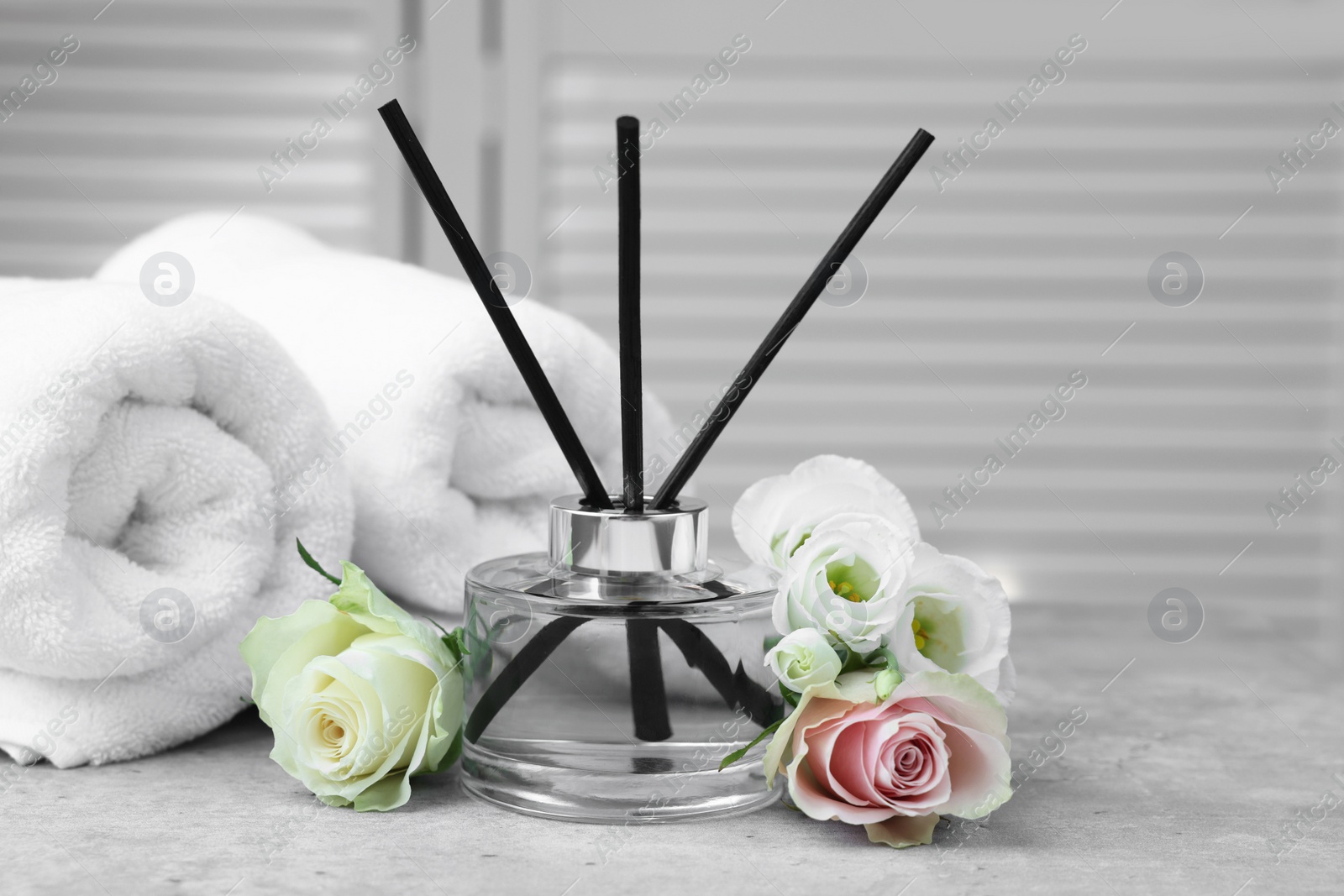 Photo of Towels, reed air freshener and flowers on grey table indoors