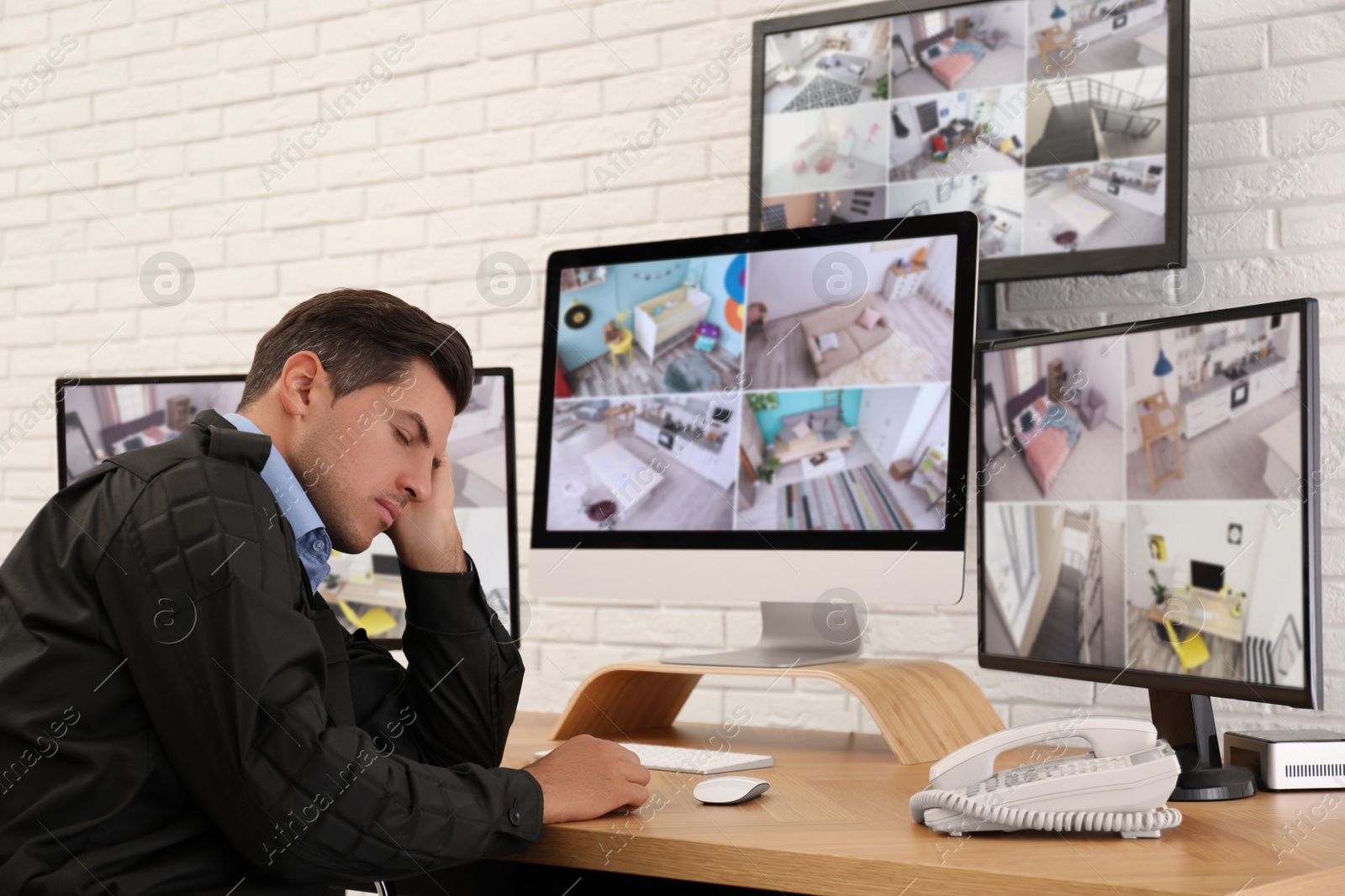 Photo of Male security guard sleeping near monitors at workplace