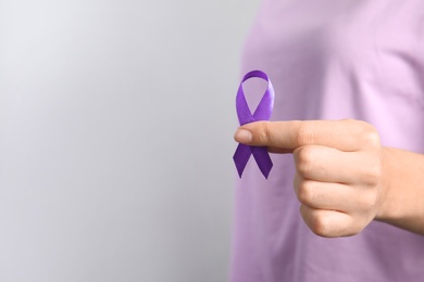 Photo of Woman holding purple ribbon on grey background, closeup with space for text. Domestic violence awareness