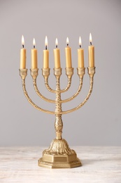 Photo of Golden menorah with burning candles on table against light grey background
