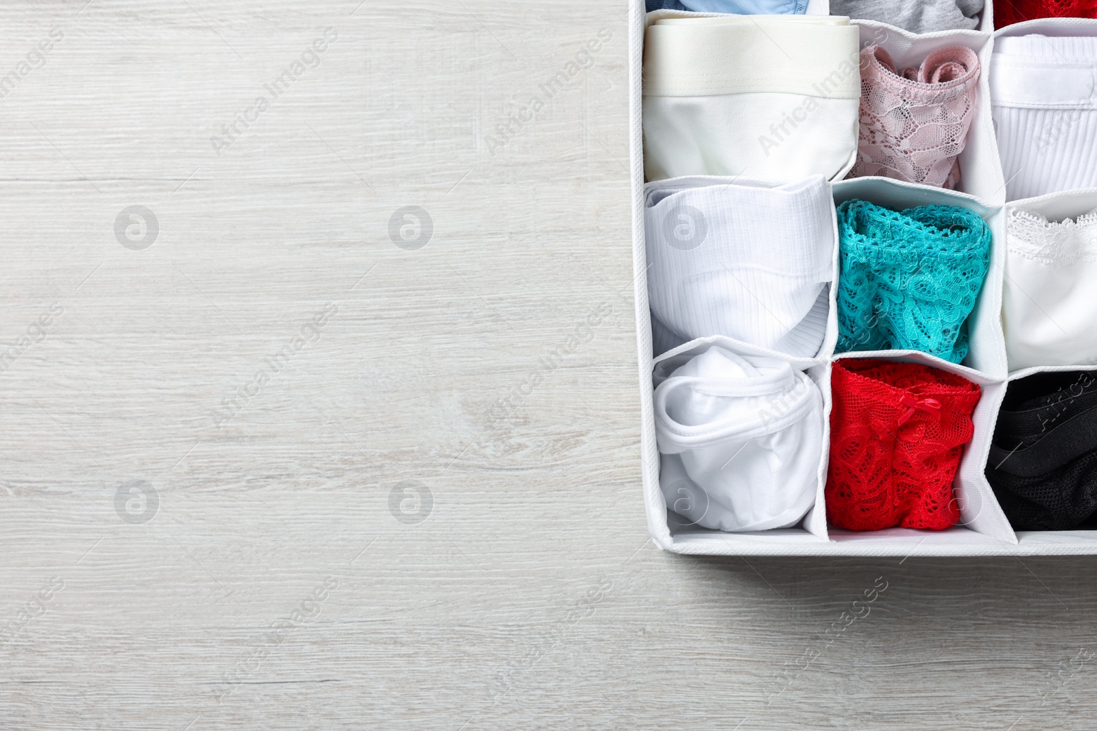 Photo of Organizer with folded women's underwear on light wooden table, top view. Space for text