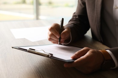 Photo of Businessman signing document at table indoors, closeup