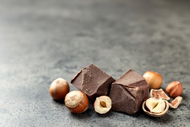 Photo of Delicious chocolate chunks and hazelnuts on grey table. Space for text