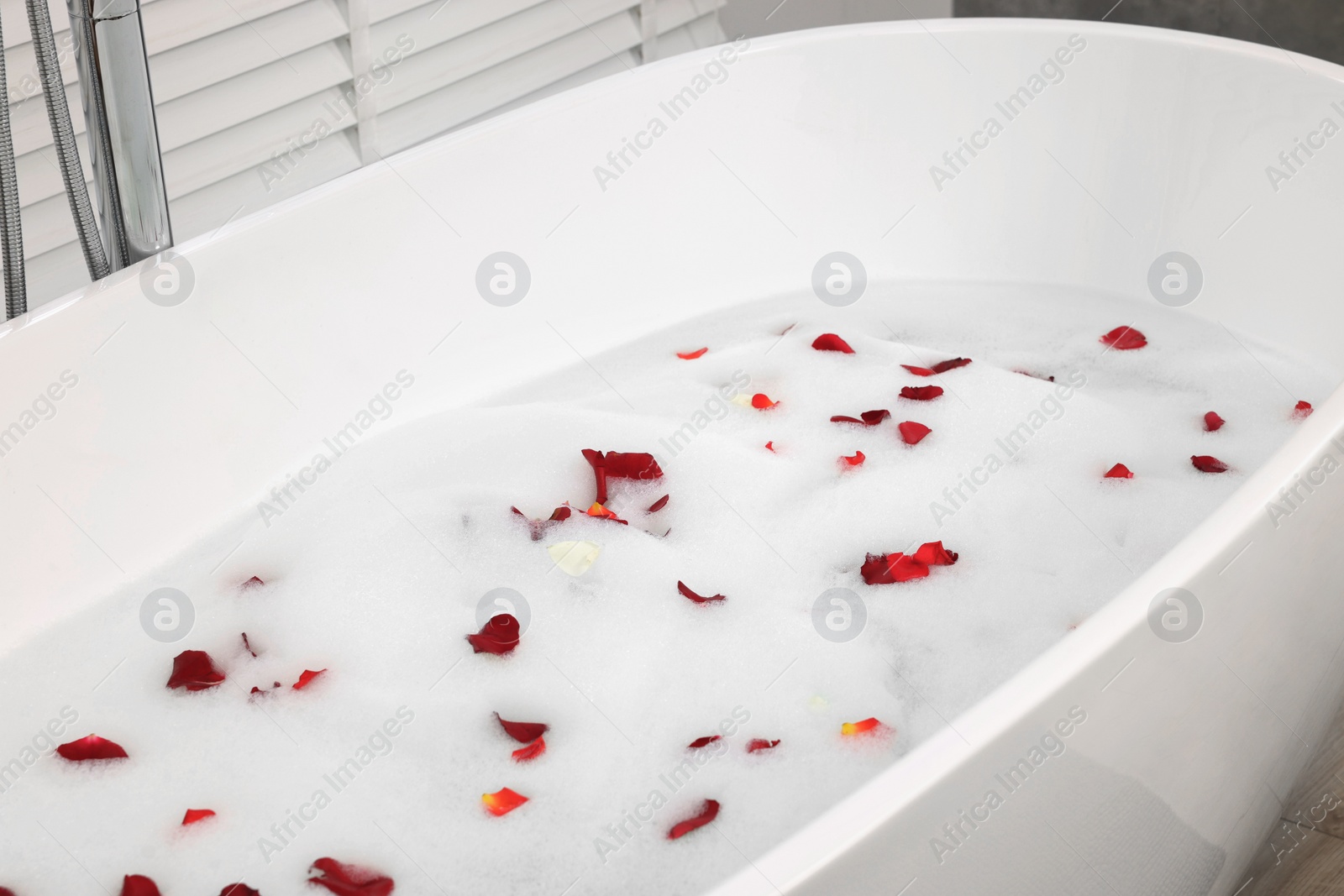 Photo of Bath tub with rose petals and foam in bathroom