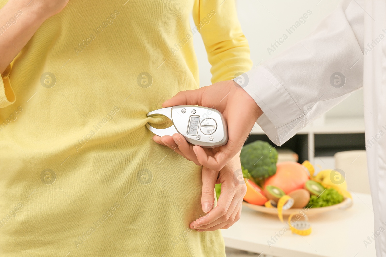 Photo of Nutritionist measuring patient's body fat with digital caliper in clinic, closeup
