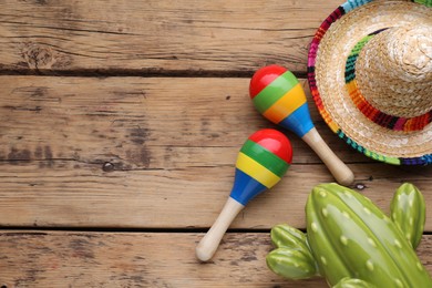 Photo of Colorful maracas, toy cactus and sombrero hat on wooden table, flat lay with space for text. Musical instrument