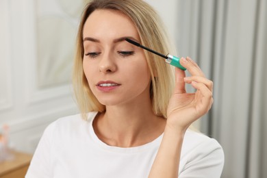 Beautiful woman applying mascara with brush indoors