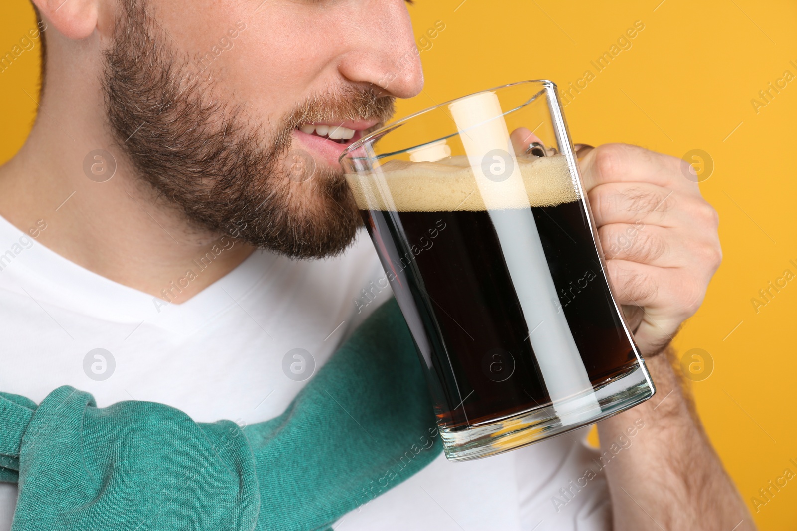 Photo of Young man with cold kvass on yellow background, closeup. Traditional Russian summer drink