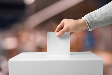 Image of Man putting his vote into ballot box indoors, closeup