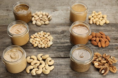 Photo of Tasty nut butters in jars and raw nuts on wooden table