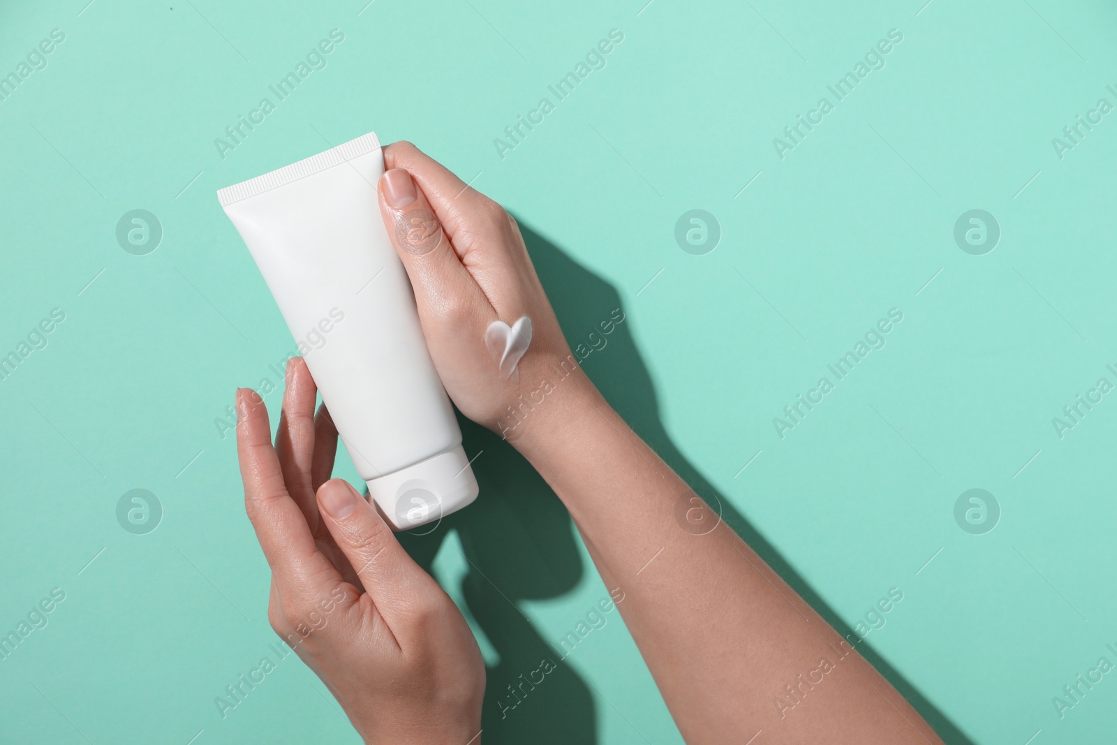 Photo of Woman with tube of hand cream on turquoise background, top view. Space for text