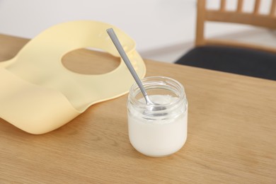 Photo of Jar of delicious yogurt with spoon and bib on wooden table