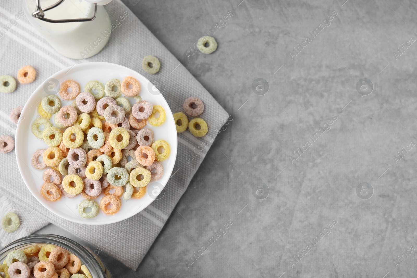 Photo of Tasty colorful cereal rings and milk in bowl on grey table, flat lay. Space for text