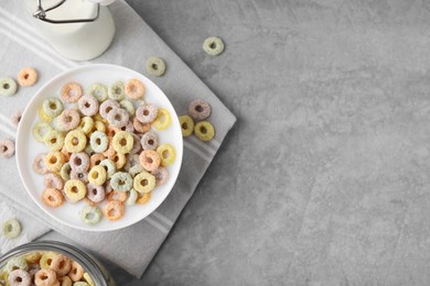 Photo of Tasty colorful cereal rings and milk in bowl on grey table, flat lay. Space for text