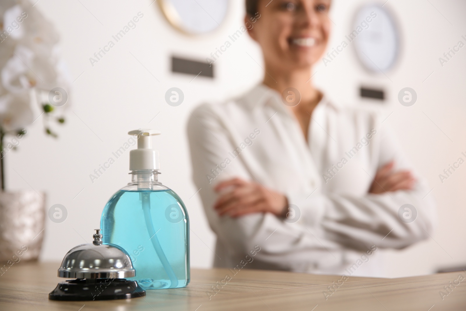 Photo of Receptionist at countertop in hotel, focus on dispenser bottle with antiseptic gel and service bell