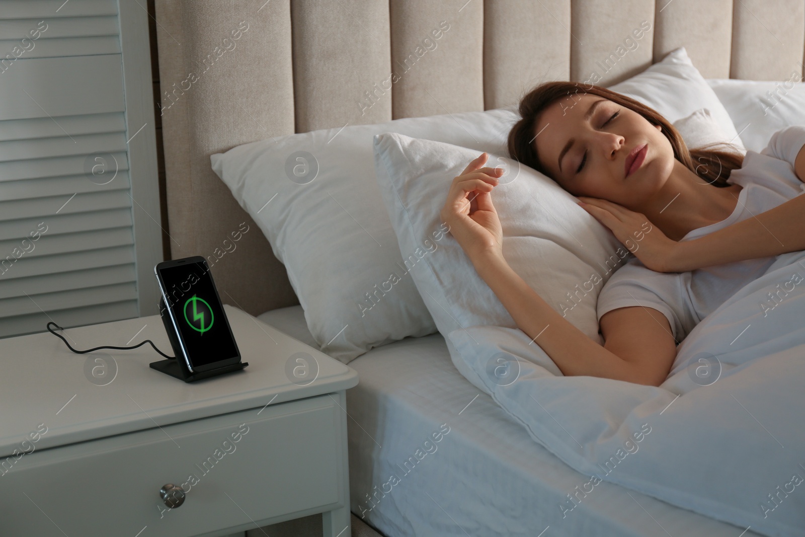 Photo of Smartphone charging on wireless pad and woman sleeping in bed