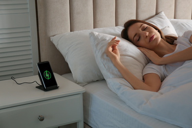 Smartphone charging on wireless pad and woman sleeping in bed