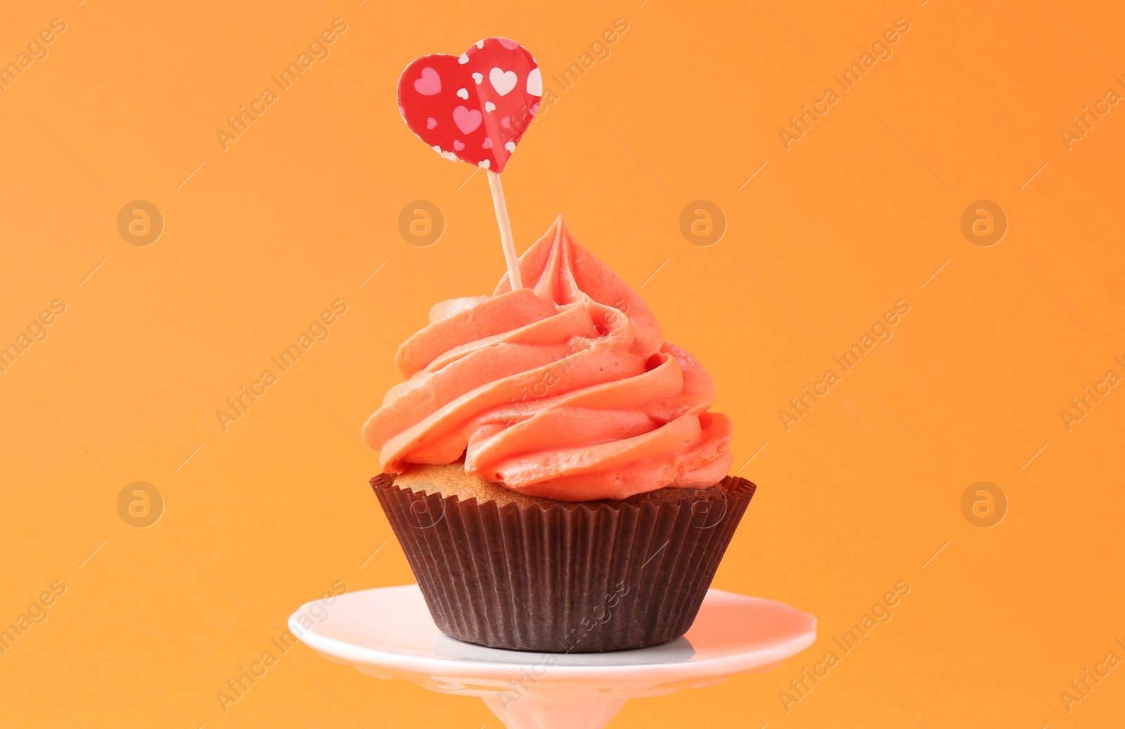 Photo of Delicious cupcake with bright cream and heart topper on orange background