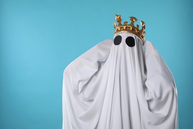 Person in ghost costume and luxurious crown on light blue background, space for text