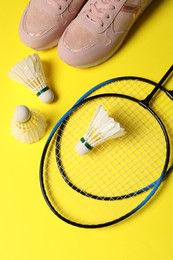 Photo of Feather badminton shuttlecocks, rackets and sneakers on yellow background, flat lay
