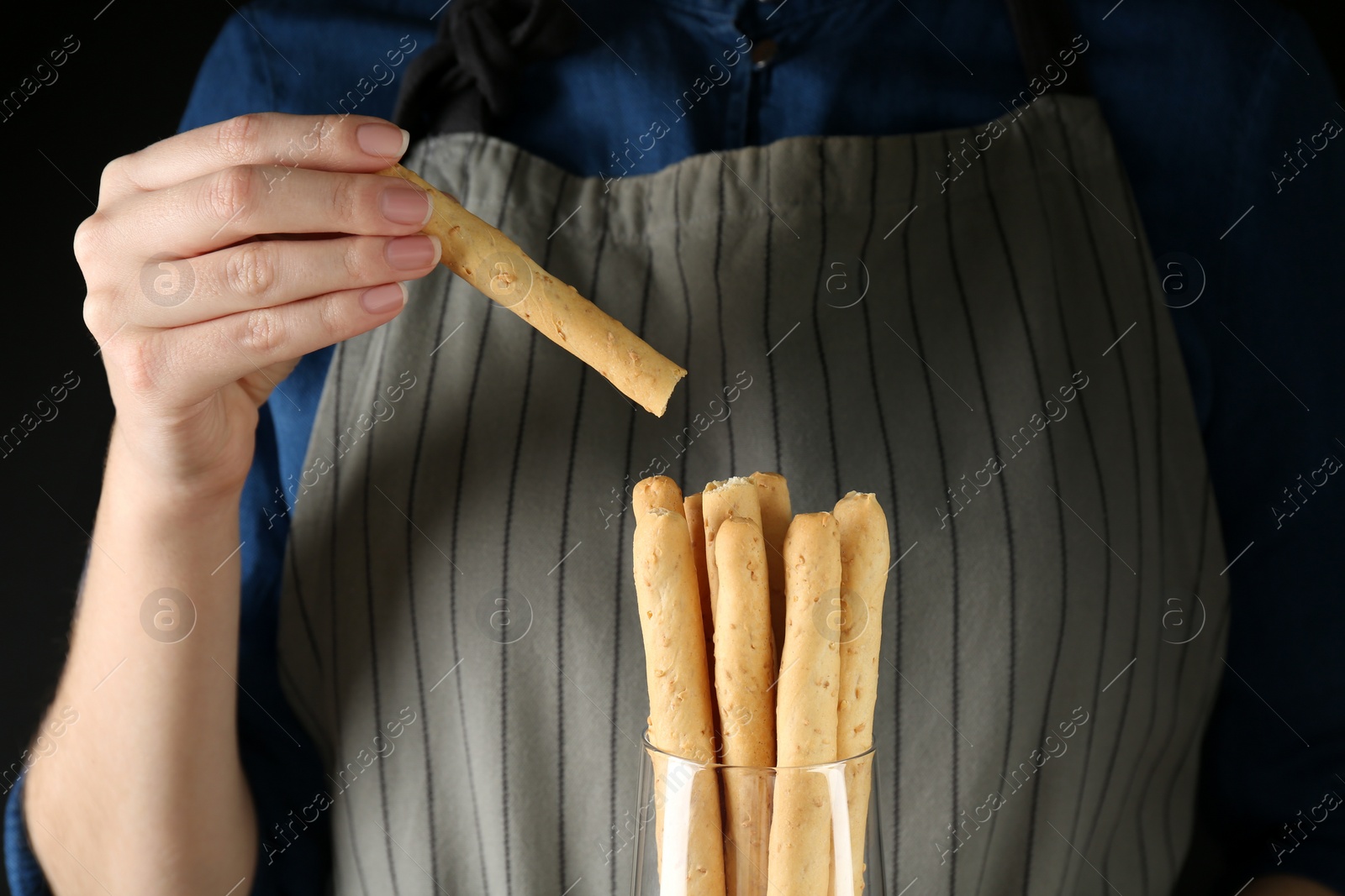 Photo of Woman taking fresh delicious grissino from glass on black background, closeup