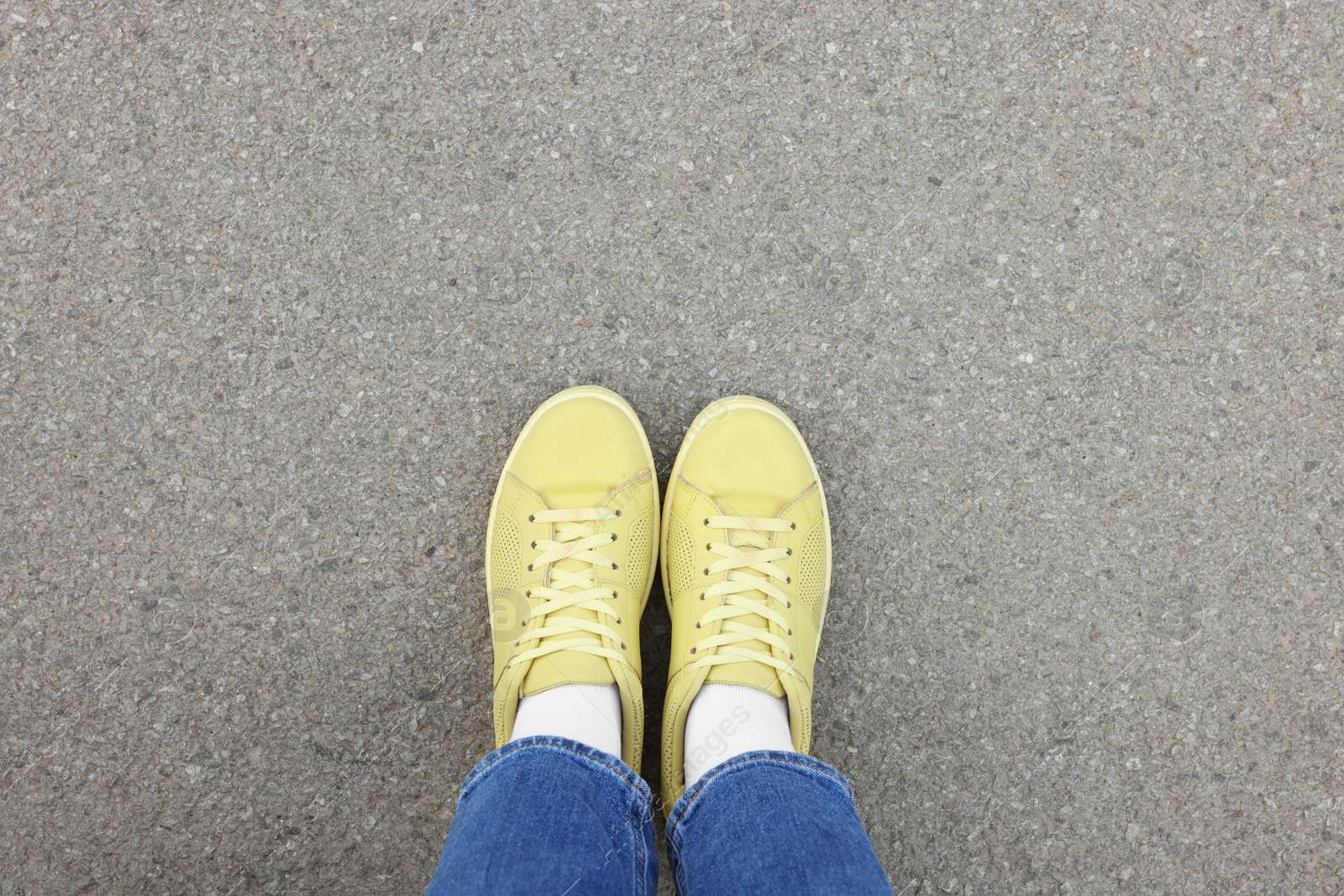 Photo of Woman in stylish gumshoes on asphalt, top view