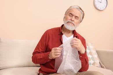 Senior man popping bubble wrap at home. Stress relief