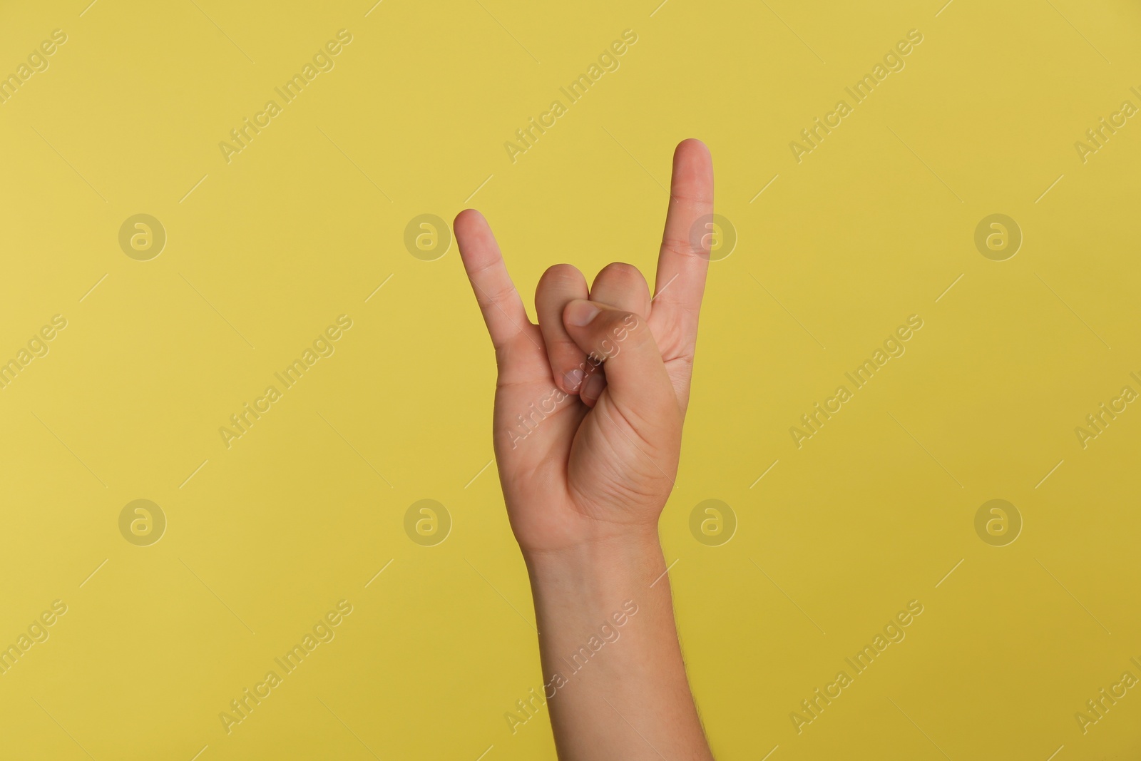 Photo of Teenage boy showing rock gesture on yellow background, closeup