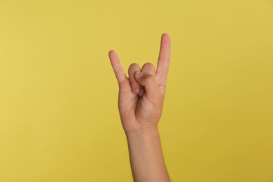 Photo of Teenage boy showing rock gesture on yellow background, closeup