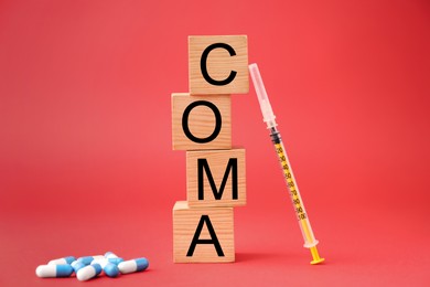 Photo of Wooden cubes with word Coma, syringe and pills on red background