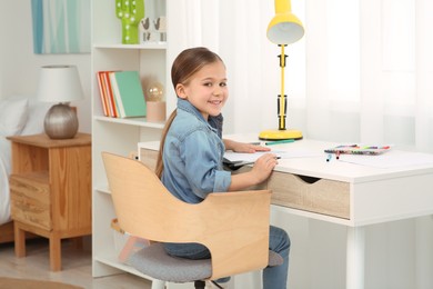 Photo of Cute little girl with colorful markers at desk in room. Home workplace