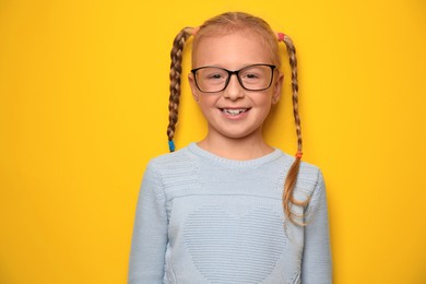 Cute little girl with braided hair and glasses on yellow background