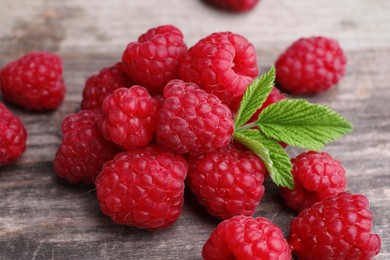 Tasty ripe raspberries and green leaves on wooden table, closeup