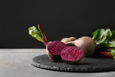 Photo of Slate board with fresh beets on grey table against black background. Space for text