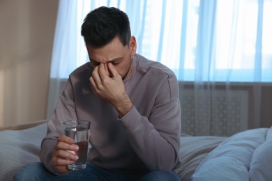 Upset man with glass of water in bedroom. Loneliness concept