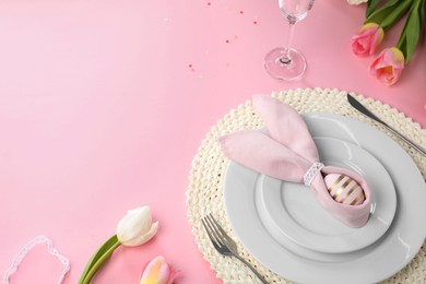 Photo of Festive table setting with painted egg, plates and tulips on pink background, space for text. Easter celebration