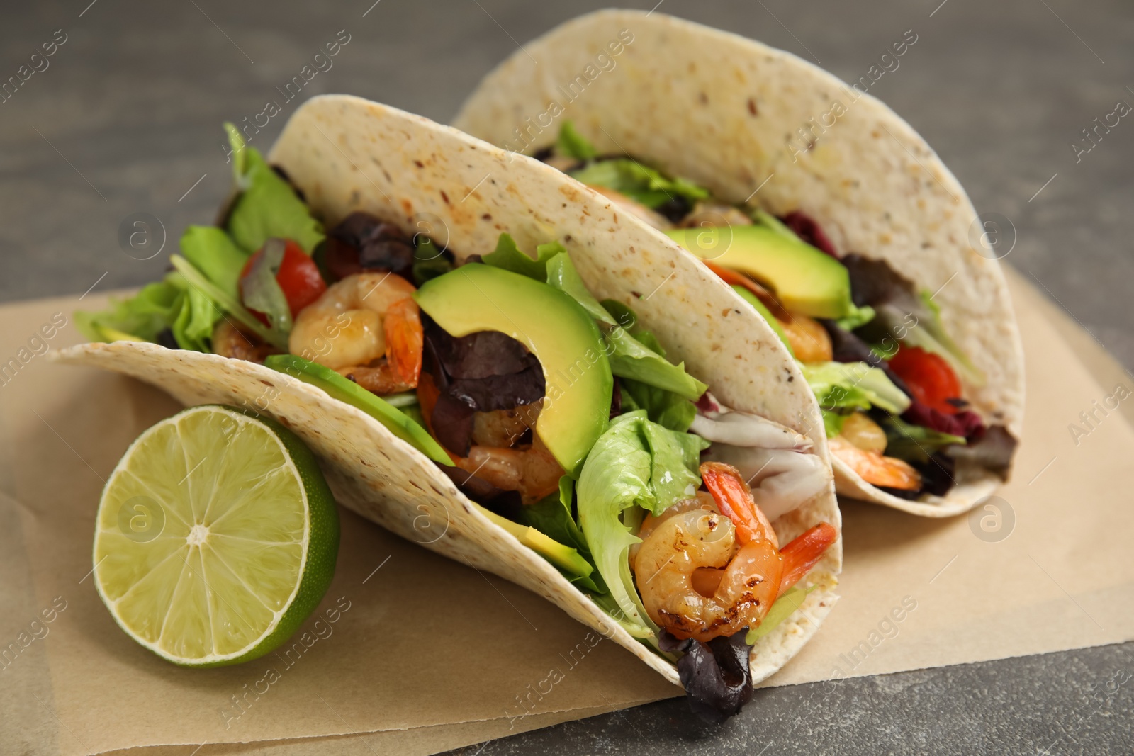 Photo of Delicious tacos with shrimps, avocado and lime on grey table, closeup