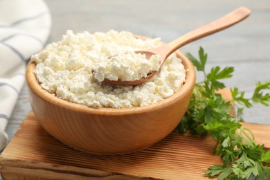 Delicious fresh cottage cheese and parsley on wooden board, closeup