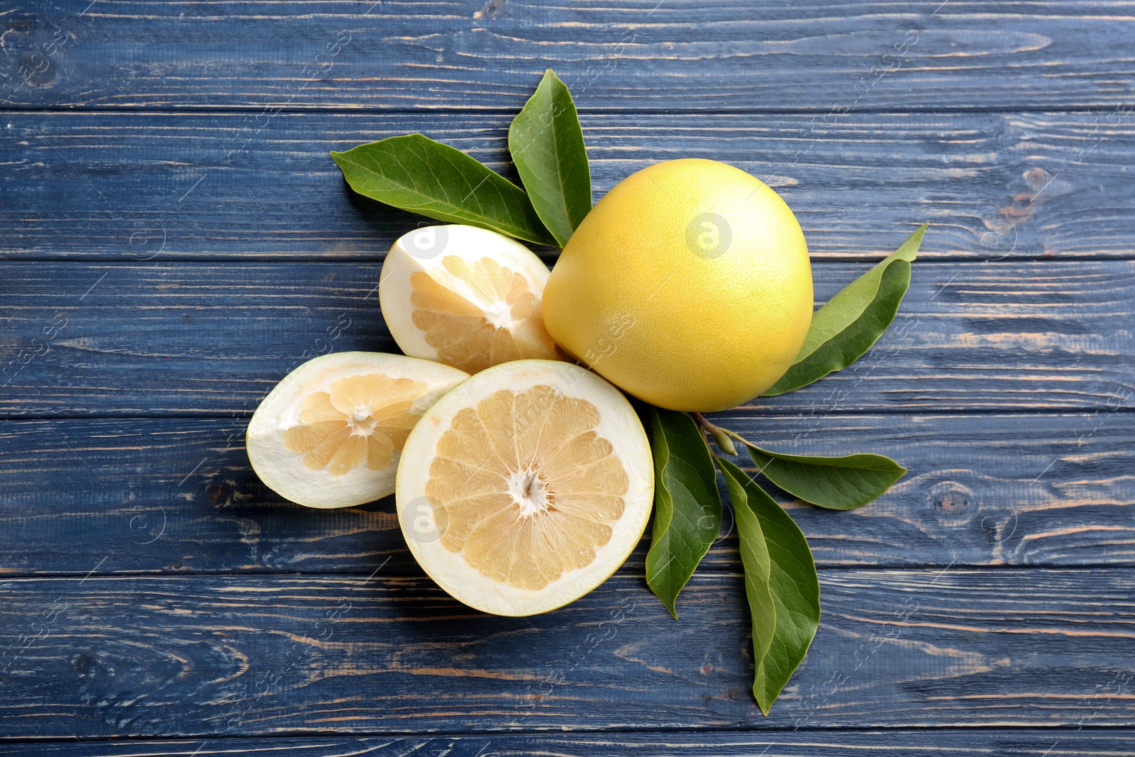 Photo of Fresh cut and whole pomelo fruits on blue wooden table, flat lay