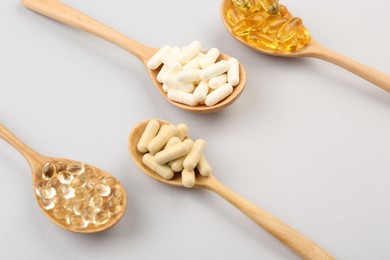 Wooden spoons with different vitamin capsules on light grey background