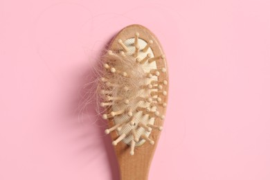 Photo of Wooden brush with lost hair on pink background, top view