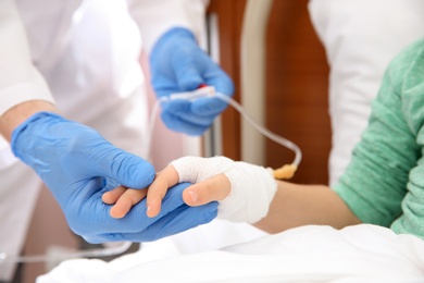 Doctor adjusting intravenous drip for little child in hospital, closeup