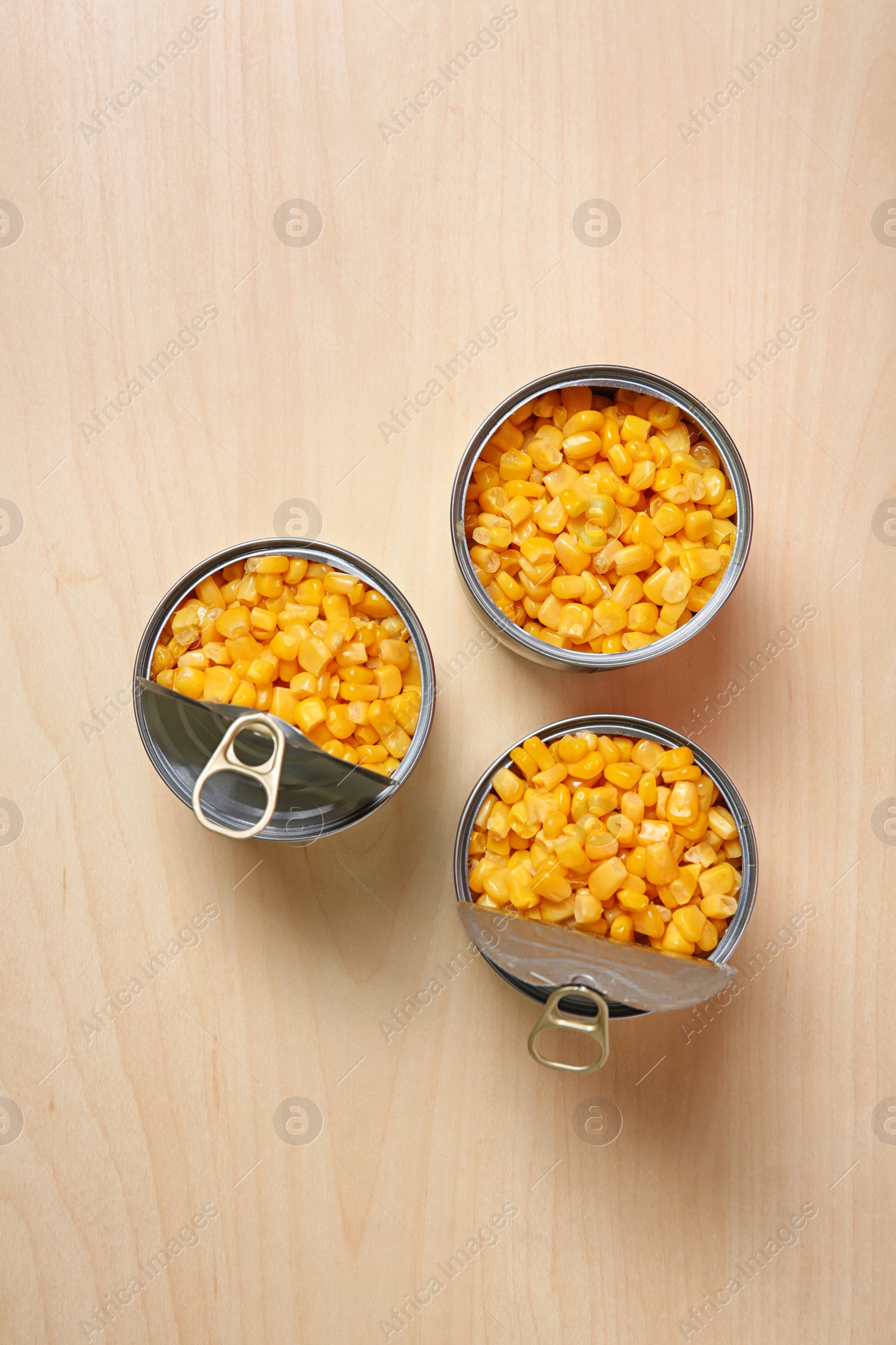 Photo of Open tin cans of sweet corn on wooden table, flat lay